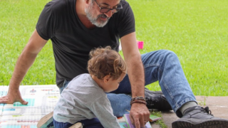Niño pequeño leyendo un libro en compañía de un adulto, representando la alfabetización en el hogar.